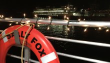 The railing of the Sally Fox is decked in holiday lights, with a Washington State Ferry in the background.