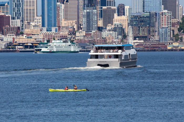 A pair of kayakers glide along Elliott Bay as King County Water Taxi's MV Doc Maynard cuts toward Downtown Seattle.