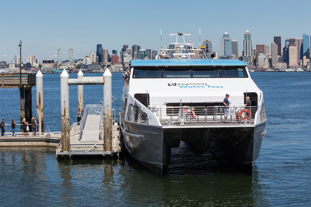 Photo of water taxi at Seacrest Dock in West Seattle on a sunny day, the Seattle skyline in the background.