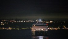 The Water Taxi glides at night through water reflecting city lights.