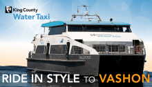 Water Taxi Sally Fox sailing into the Vashon Ferry Terminal. King County Water Taxi logo in the top left and Ride in Style to Vashon across the bottom