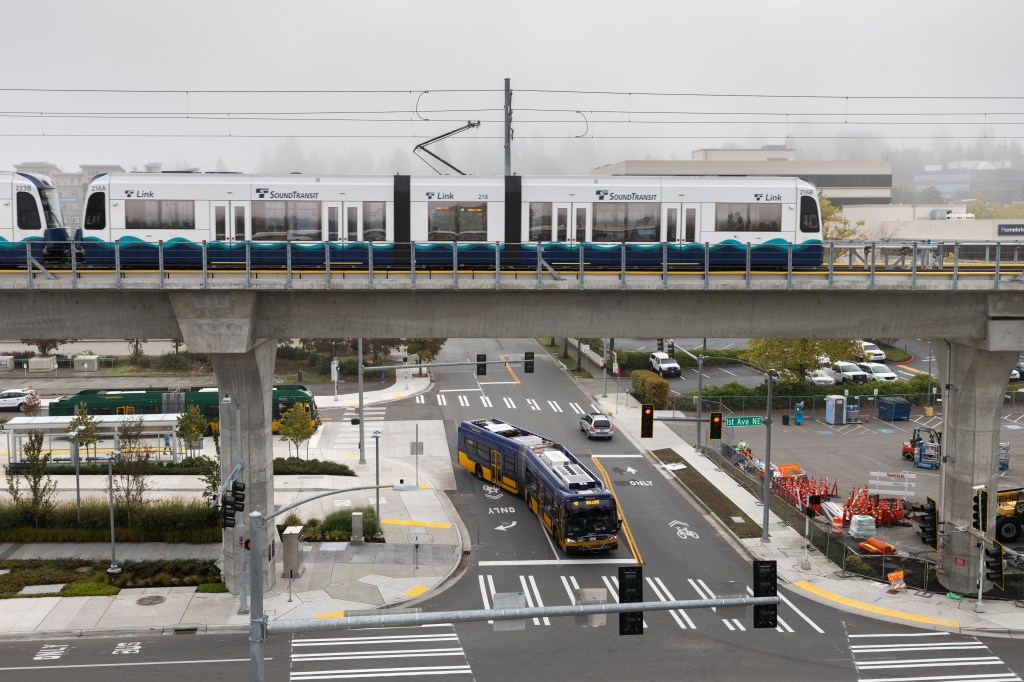 A sound light-rail train leaves the Northgate station as a King County Metro bus passes underneath